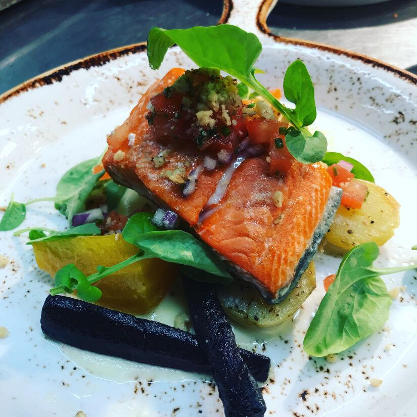 A dish showcasing a grilled fish served alongside a vibrant mix of seasonal vegetables on a white plate.