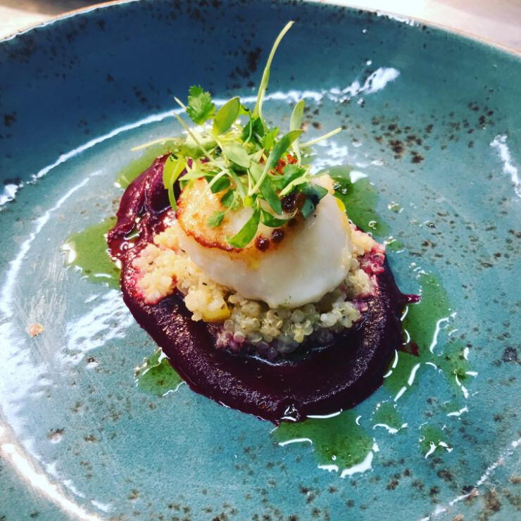 A blue plate featuring a beautifully arranged scallop garnished with vibrant beetroot slices.